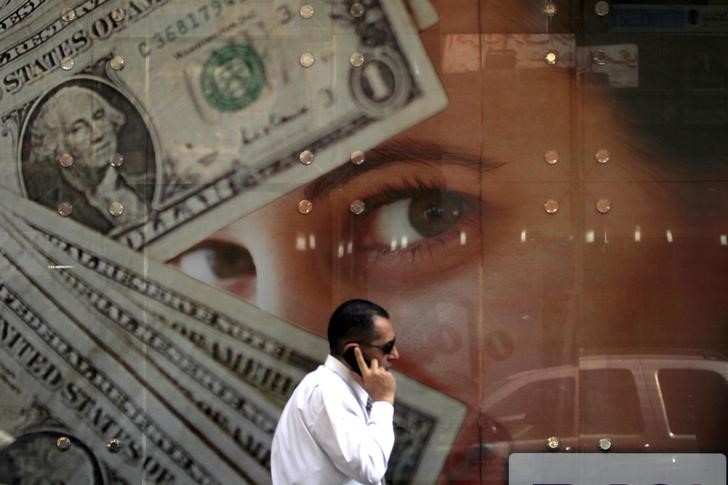 A man talks on his mobile phone as he walks past an exchange bureau advertisement showing images of the U.S dollar, in Cairo March 10, 2014. REUTERS/Amr Abdallah Dalsh